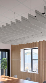 Multiple gray curved acoustic baffle panels suspended from ceiling in office space with wooden wall paneling and windows.