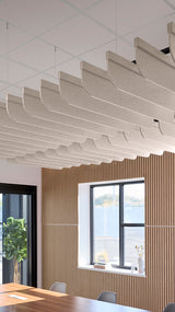 Beige acoustic fin baffles suspended from ceiling in staggered rows above wooden wall paneling and windows.