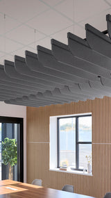 Row of curved dark gray acoustic baffles suspended from ceiling above wooden wall paneling and window.