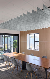 A modern conference room with a long wooden table, gray chairs, a slatted wood wall, and a large sculptural cloud-like pendant light hanging from the ceiling.