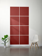 Red geometric wall art panel on a white wall with a plant and chair in the foreground.