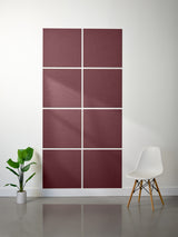 Red geometric wall art panel on a white wall with a plant and chair in the foreground.