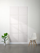 White wall with square panels, a white chair, and a potted plant on a gray floor.