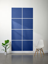 Blue wall art with geometric design on a white wall, accompanied by a plant and chair.