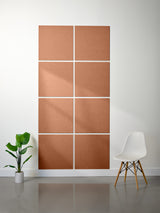 Brown square panels on a white wall with a white chair and plant in the foreground.