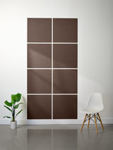 Brown abstract wall panels on a white wall with a plant and chair in the foreground