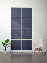 Nine square dark blue panels on a white wall with a plant and chair in the foreground.