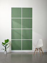 Four-by-two grid of green tiles with engraved arch and line patterns, displayed on wall above white chair.
