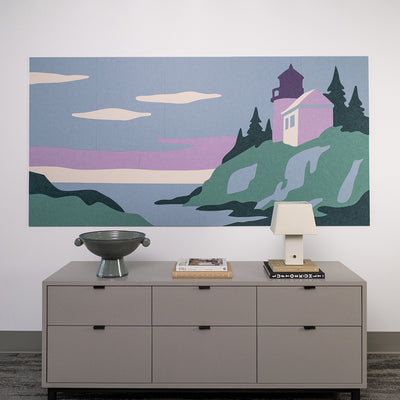 Decorative painting of a lighthouse on a wall above a dresser with a lamp and books.