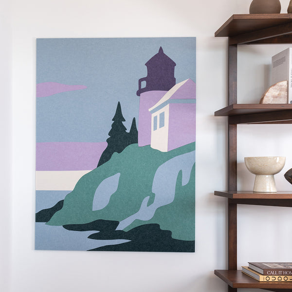 Acoustic felt art of a lighthouse scene on a wall next to a wooden shelf.
