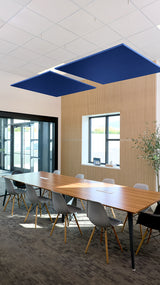 Two navy blue square acoustic baffles suspended from ceiling above conference table in office space.