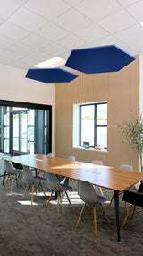 Two dark blue hexagonal acoustic panels suspended from ceiling above conference table in office space.