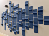 Blue dimensional tiles arranged in varying depths and sizes on a beige wall, creating a 3D geometric pattern.