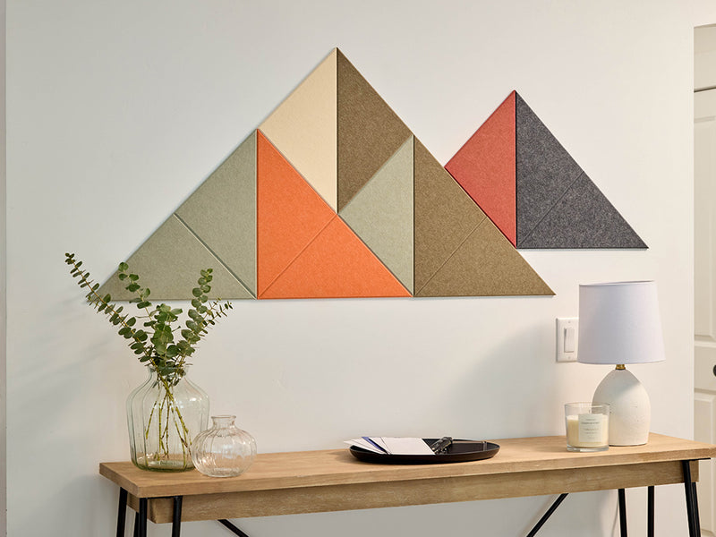 Geometric wall art with triangles in various colors on a white wall above a wooden table.