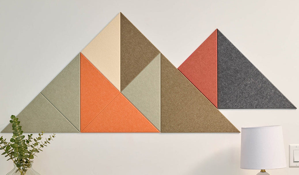 Geometric wall art with triangles in various colors  in the shape of a mountain on a white wall above a wooden table.