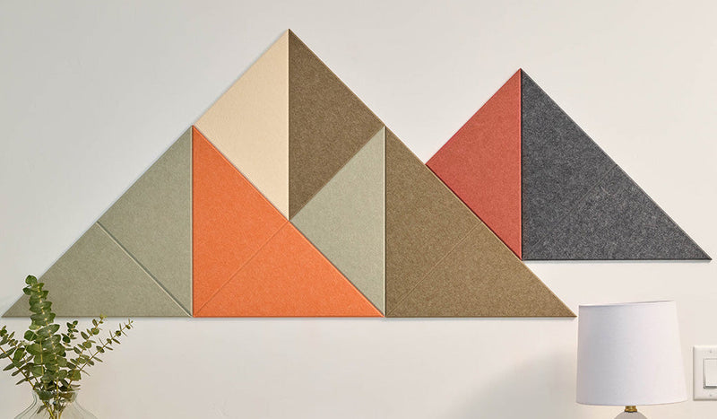 Geometric wall art with triangles in various colors  in the shape of a mountain on a white wall above a wooden table.