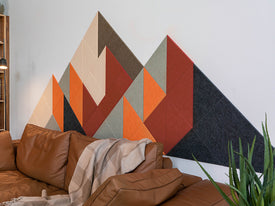 Geometric wall art with triangles in various colors on a white wall above a brown sofa.