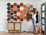 Woman hanging a coat on a hexagonal patterned wall in a home setting.