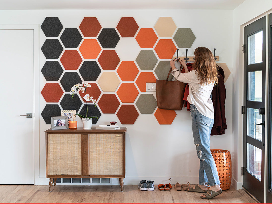Woman hanging a coat on a hexagonal patterned wall in a home setting.