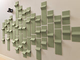 Sage green dimensional wall tiles arranged in varied heights and depths creating a textured 3D pattern on a neutral wall.