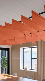 Orange angled acoustic baffles suspended from ceiling in office space above wooden slat wall.