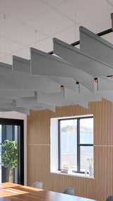Gray angled acoustic baffles suspended from ceiling grid in modern office space above wooden wall paneling.