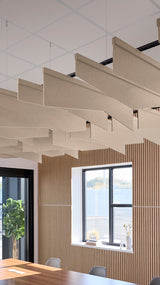 Angled acoustic baffles in beige fabric suspended from ceiling in modern office space with wood wall paneling.