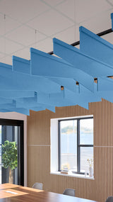 Blue angled acoustic baffles suspended from ceiling in modern office space with wood paneling and windows.
