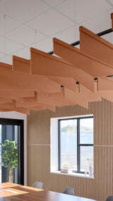 Terracotta angled acoustic baffles suspended from ceiling in modern office space with windows and wooden wall paneling.