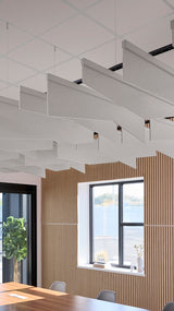Multiple angled gray acoustic baffles suspended from ceiling in modern office space with wood paneling and windows.