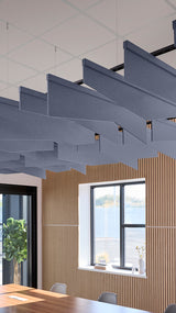 Blue-gray angled acoustic baffles suspended from ceiling in modern office space with wood paneling and windows.