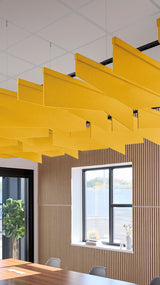 Yellow angled acoustic baffles suspended from ceiling in office space with suspended suspension cables.