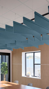 Multiple teal angled acoustic baffles suspended from ceiling in modern office space above wooden wall paneling.