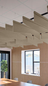 Angled acoustic baffles in beige fabric suspended from ceiling in modern office space with wood paneling and windows.