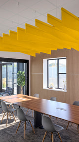 Yellow angled acoustic blade baffles suspended from ceiling in modern office conference room above wooden table.