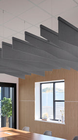 Five dark gray angled acoustic baffles suspended from a ceiling grid in an office space with wood paneling.