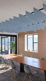 Blue angled acoustic baffles suspended from ceiling in modern office space above wooden conference table.