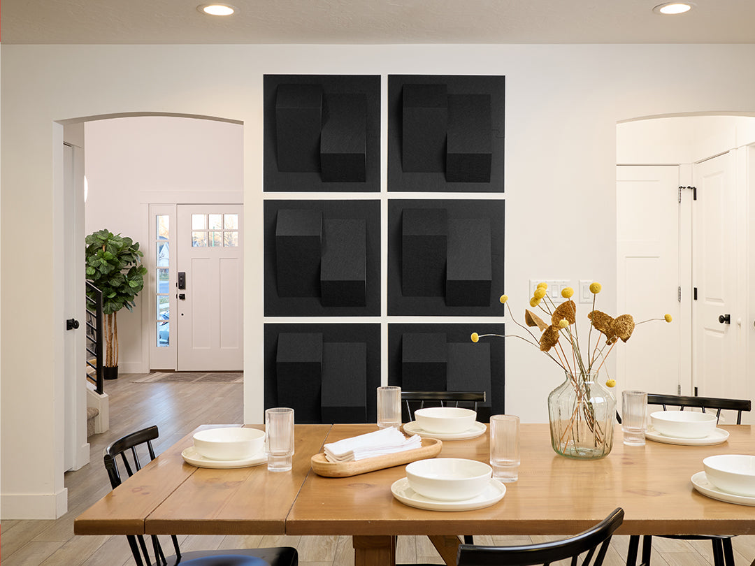 Dining room with a wooden table set for a meal, black acoustic wall art, and a vase with flowers.