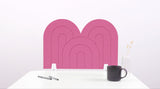Pink arch-shaped desk divider with nested geometric patterns, displayed on white desk with black mug and pens.