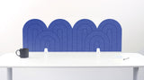 A dark blue felt desk divider with a wavy, layered arch pattern, shown standing behind a white desk with a black mug on the left and a notepad on the right.