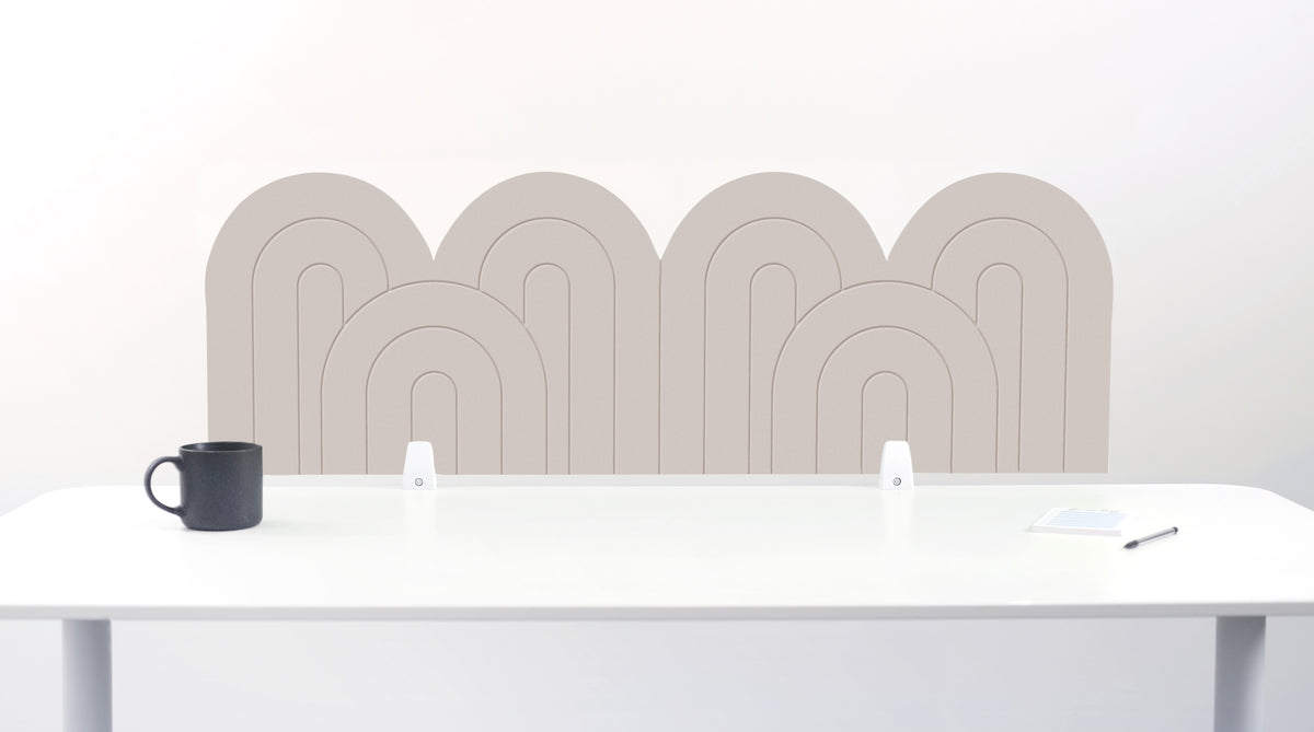 A white felt desk divider with a wavy, layered arch pattern, shown standing behind a white desk with a black mug on the left and a notepad on the right.