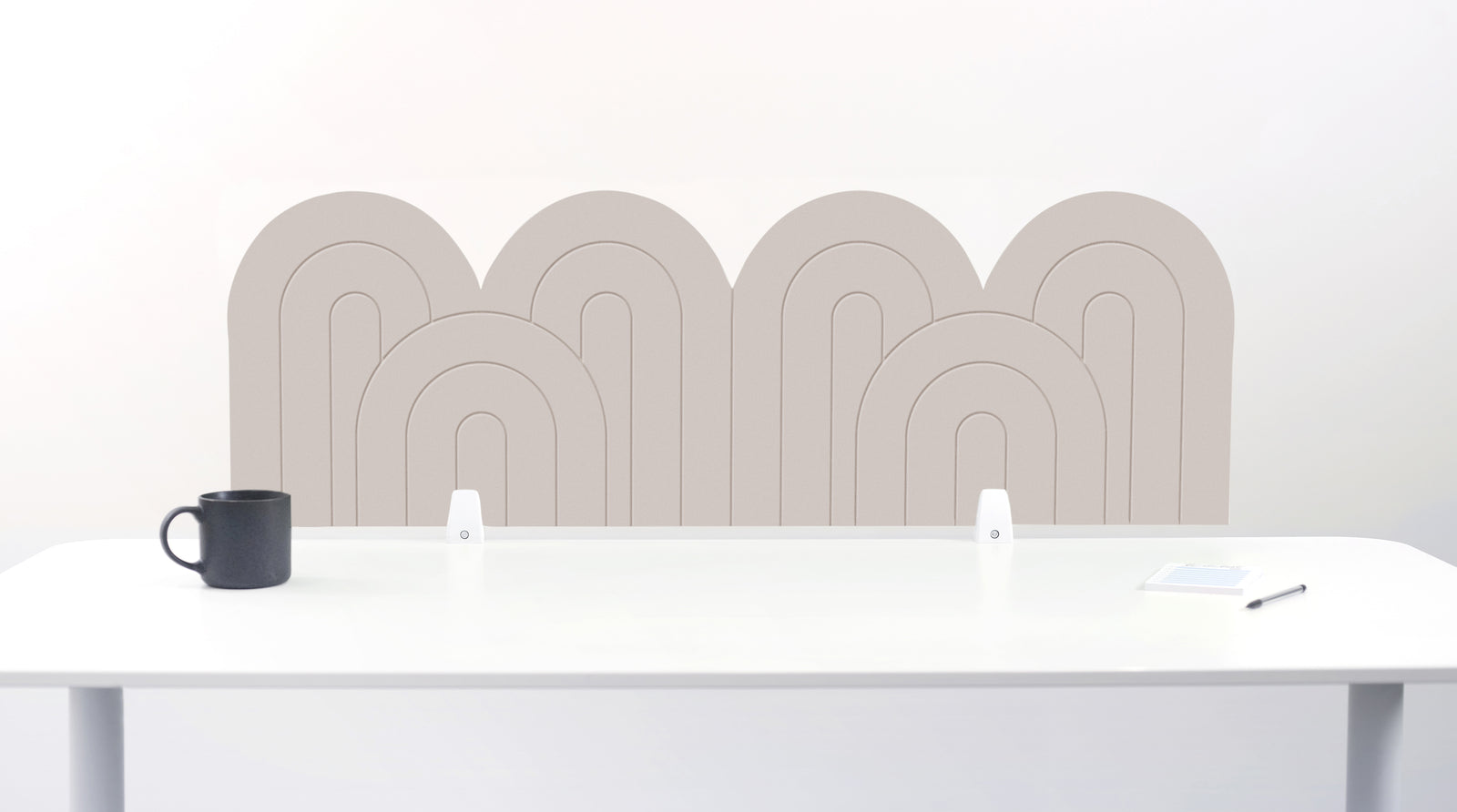 A white felt desk divider with a wavy, layered arch pattern, shown standing behind a white desk with a black mug on the left and a notepad on the right.