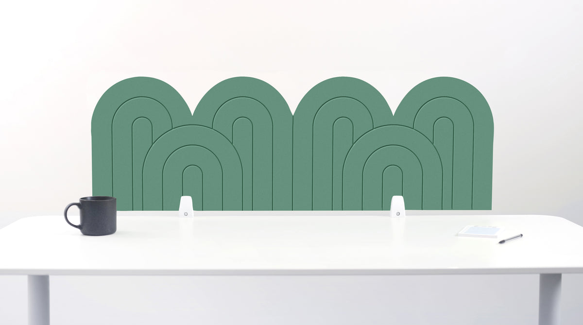 A mint felt desk divider with a wavy, layered arch pattern, shown standing behind a white desk with a black mug on the left and a notepad on the right.