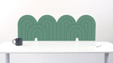 A mint felt desk divider with a wavy, layered arch pattern, shown standing behind a white desk with a black mug on the left and a notepad on the right.