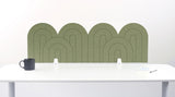 An olive felt desk divider with a wavy, layered arch pattern, shown standing behind a white desk with a black mug on the left and a notepad on the right.