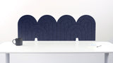 A navy blue felt desk divider with a wavy, layered arch pattern, shown standing behind a white desk with a black mug on the left and a notepad on the right.