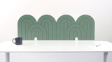 A long green palm felt desk divider with a wavy, layered arch pattern, shown standing behind a white desk with a black mug on the left and a notepad on the right.