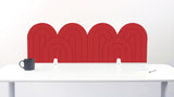 An red felt desk divider with a wavy, layered arch pattern, shown standing behind a white desk with a black mug on the left and a notepad on the right.