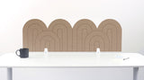 A light brown felt desk divider with a wavy, layered arch pattern, shown standing behind a white desk with a black mug on the left and a notepad on the right.