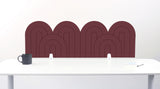A brown felt desk divider with a wavy, layered arch pattern, shown standing behind a white desk with a black mug on the left and a notepad on the right.